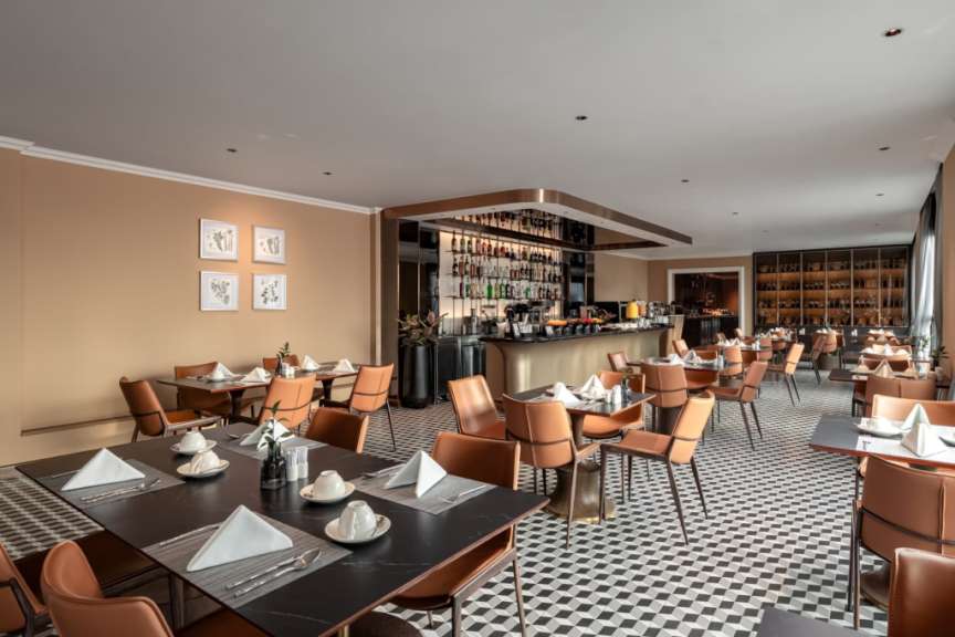 Das Bild zeigt ein stilvolles Restaurant mit braunen Ledersesseln, kariertem Boden und einer Bar im Hintergrund.