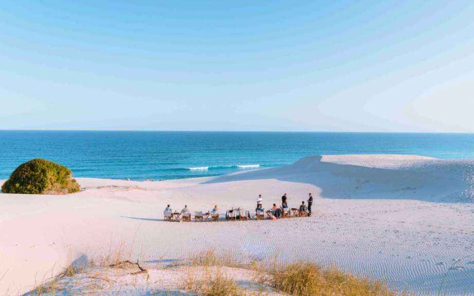 Eine Gruppe von Menschen sitzt auf einer Düne mit Blick auf das Meer