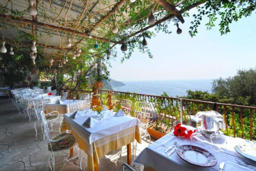 Ein Außenbereich eines Restaurants mit gedeckten Tischen und Blick auf das Meer.