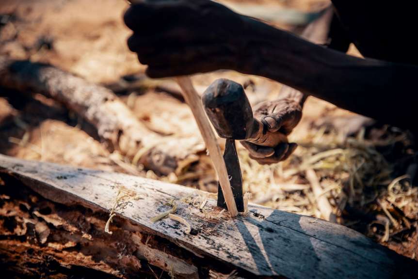 Ein Mann formt mit einem Hammer und einem Stechbeitel ein Stück Holz.