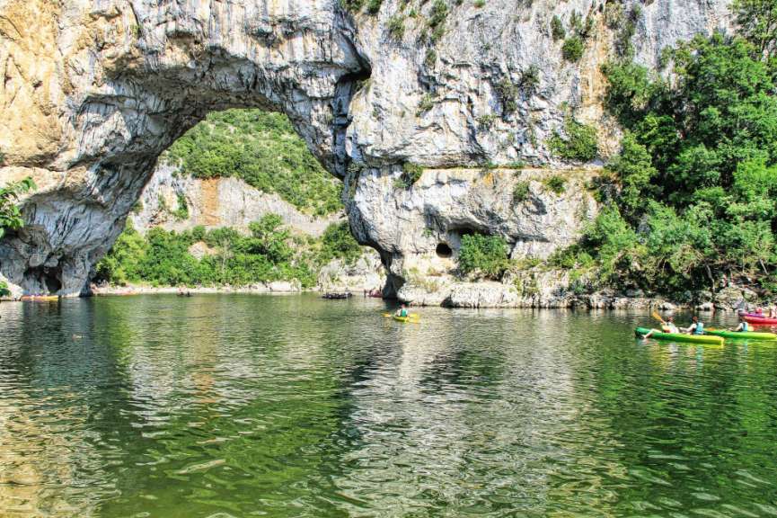 Eine Gruppe von Menschen paddelt auf einem See unter einem Felsbogen