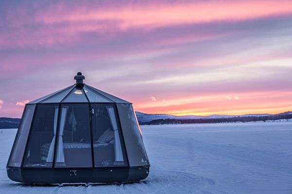 Ein Zelt steht inmitten eines schneebedeckten Feldes bei Sonnenuntergang