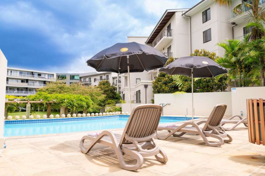 Liegestühle und Sonnenschirme neben einem Pool mit einem Gebäude im Hintergrund
