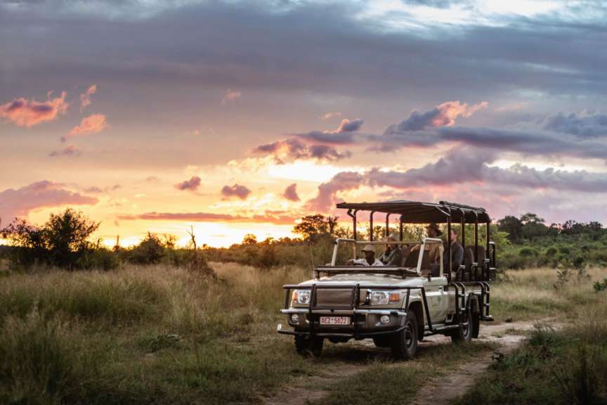 Ein jeep fährt auf einer unbefestigten straße in der savanne bei sonnenuntergang