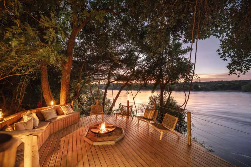 Ein Holzdeck mit einem Feuer und Stühlen über einem Fluss