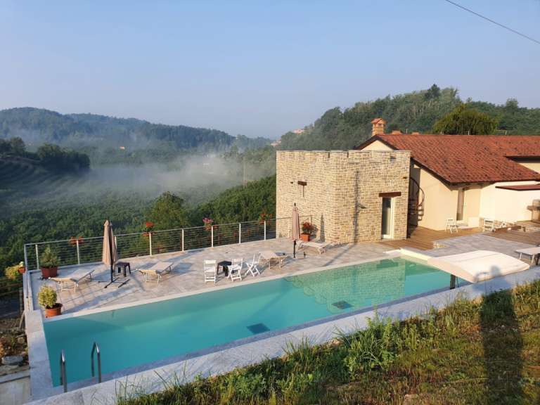 Ein Pool mit Blick auf neblige Hügel und ein Steingebäude mit rotem Ziegeldach.