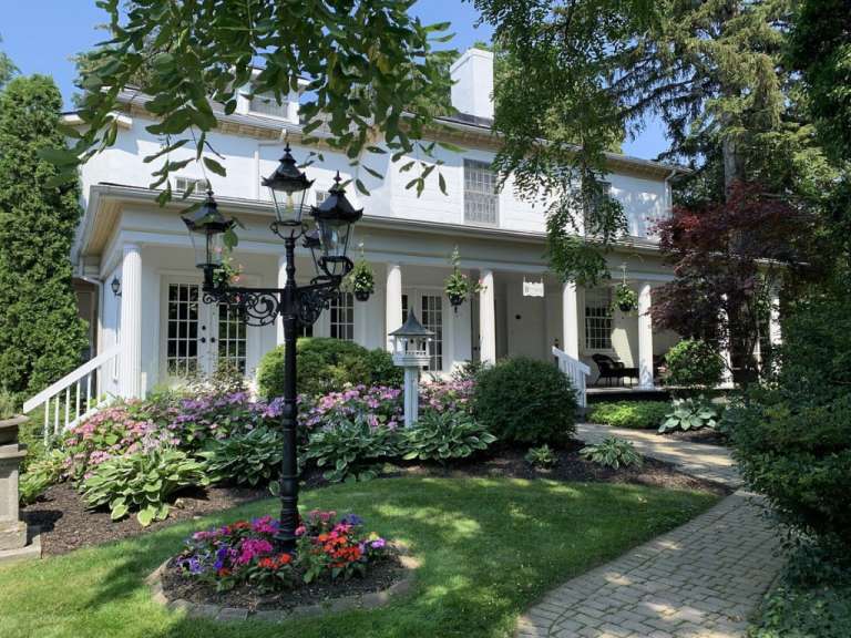 Ein großes weißes Haus mit einer Veranda und einem Blumenbeet