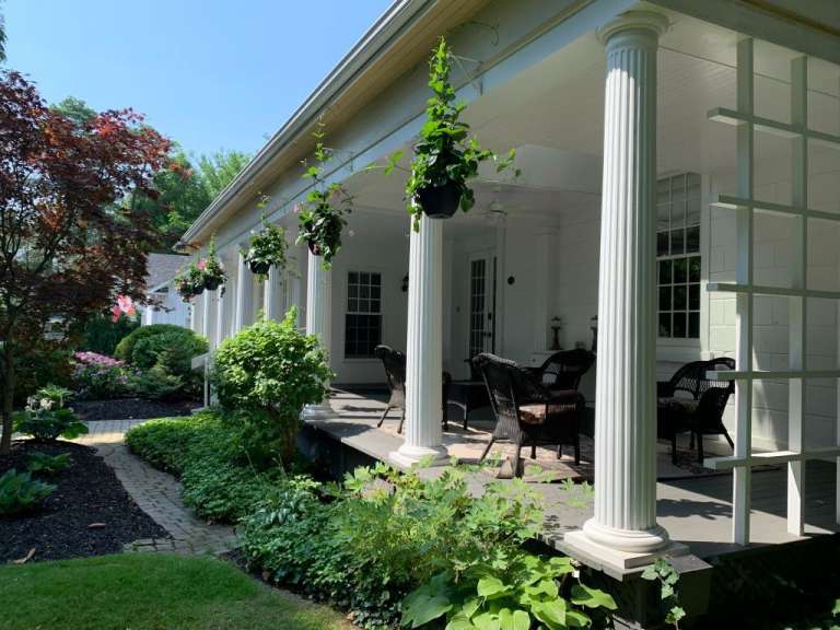 Ein weißes Haus mit einer Veranda und Stühlen darauf