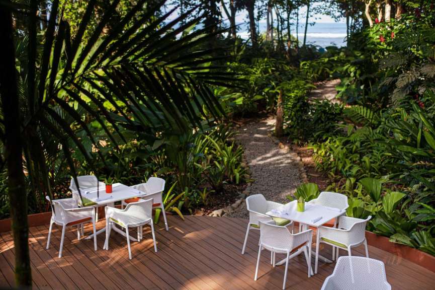 Eine Terrasse mit weißen Tischen und Stühlen inmitten eines tropischen Dschungels