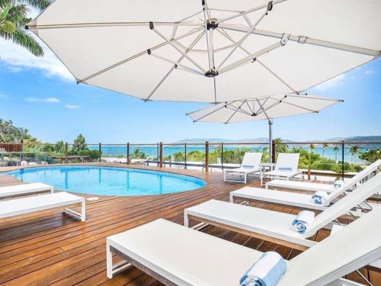 Liegestühle und Sonnenschirme um einen Pool auf einem Holzdeck