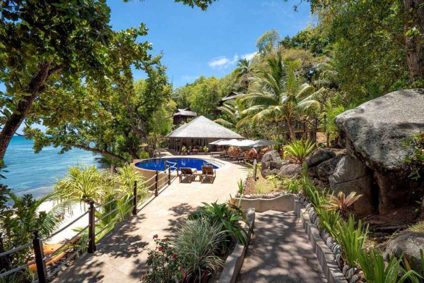 Ein Blick auf einen Poolbereich mit tropischer Vegetation und dem Meer im Hintergrund.