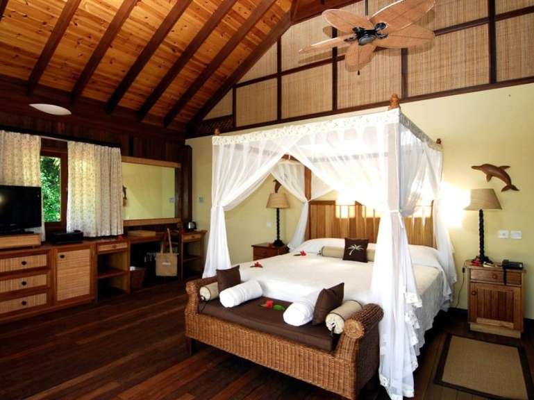 Ein geräumiges Schlafzimmer mit Himmelbett, Holzdecken und einem Fernseher.