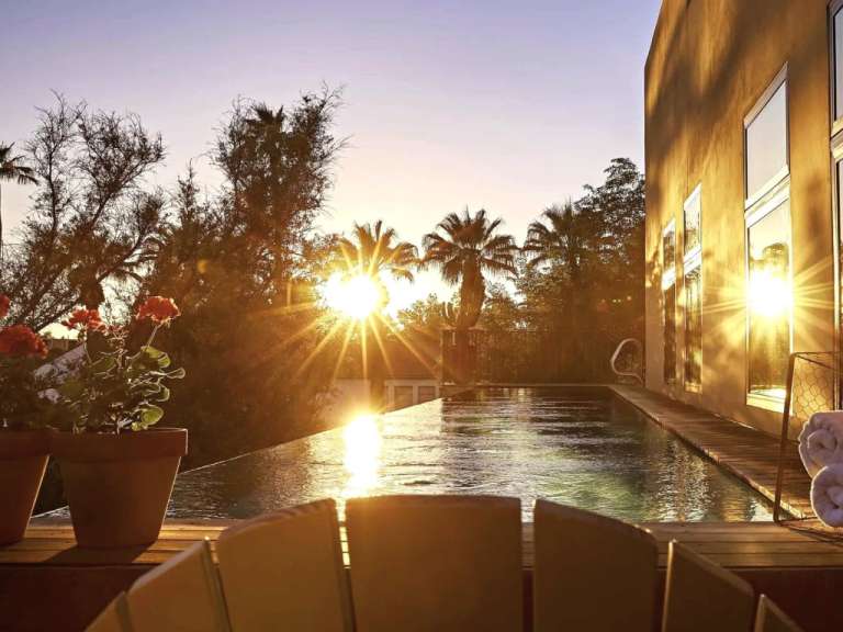 Die Sonne geht über einem Swimmingpool mit Palmen im Hintergrund