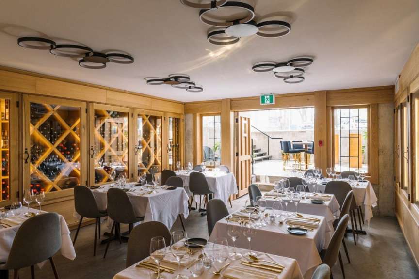 Ein elegant gedeckter Speisesaal in einem Restaurant mit Holzwänden, einer Weinvitrine und modernen Deckenleuchten.
