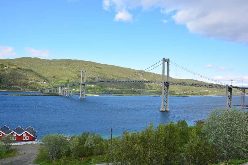 Eine Brücke über einen großen See mit einem roten Haus im Vordergrund
