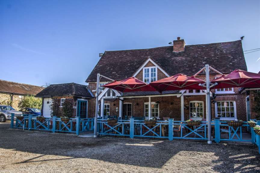 Ein Ziegelgebäude mit roten Sonnenschirmen und einer blauen Holzabsperrung im Freien.