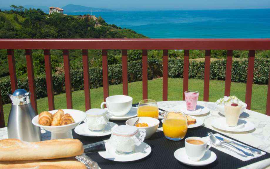 Ein Tisch mit Essen und Getränken auf einem Balkon mit Blick auf den Ozean