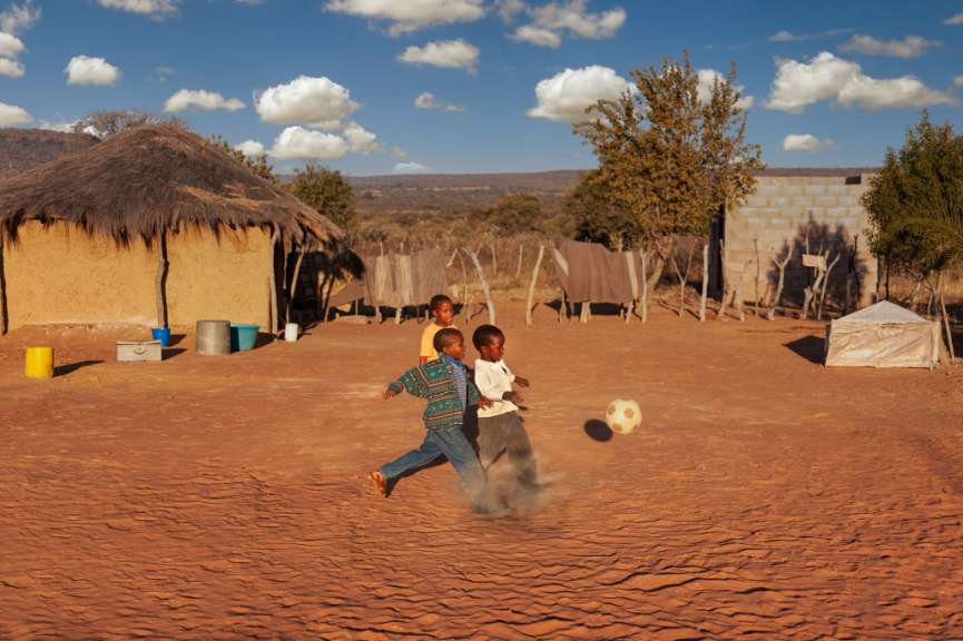 Drei Kinder spielen mit einem Fußball auf einem Feld