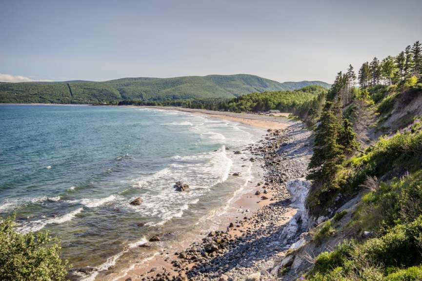 Ein felsiger Strand mit Bäumen und Bergen im Hintergrund
