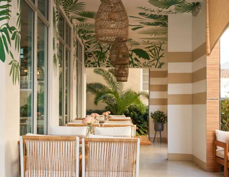 Eine Terrasse mit Tisch und Stühlen und einem Wandbild mit Palmblättern