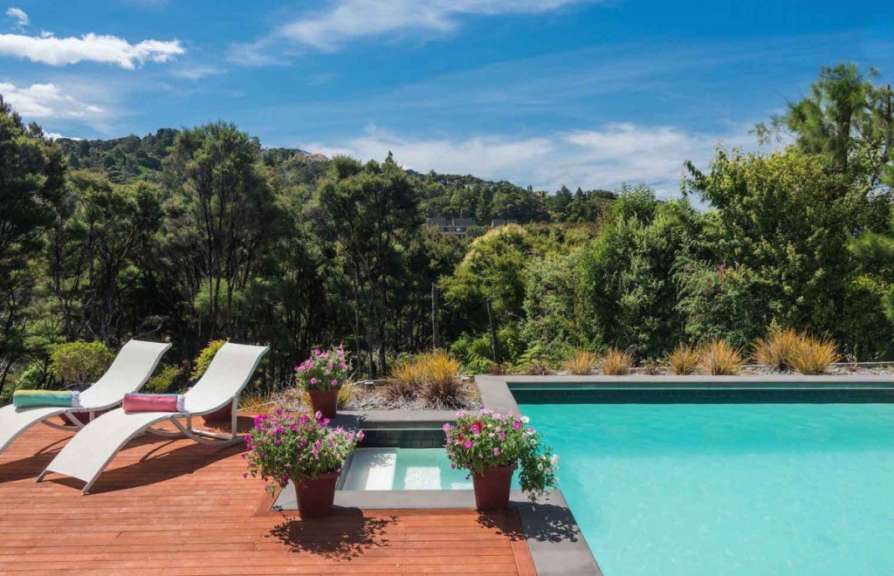 Liegestühle auf einem Holzdeck neben einem Pool mit Bäumen im Hintergrund