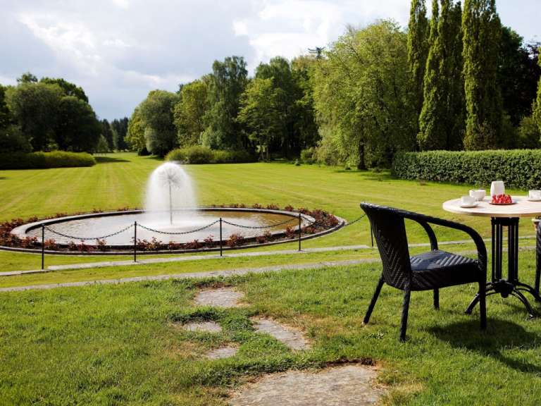 Ein Tisch und ein Stuhl in einem Park mit einem Brunnen im Hintergrund