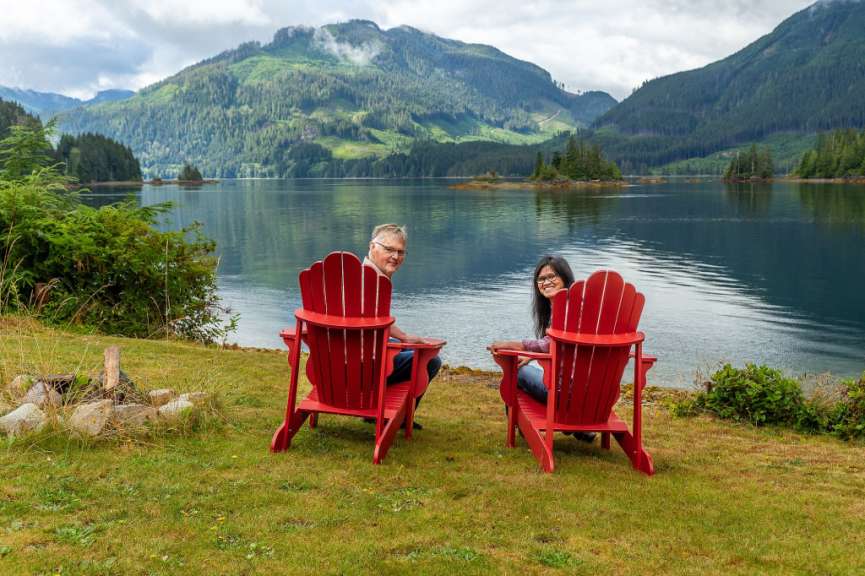 Ein Mann und eine Frau sitzen in roten Stühlen am Ufer eines Sees