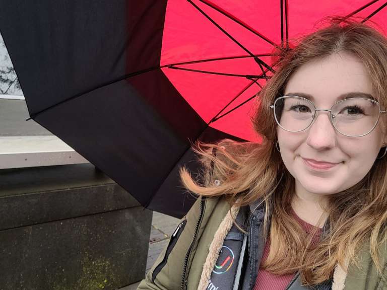 Eine junge frau mit brille steht unter einem roten regenschirm