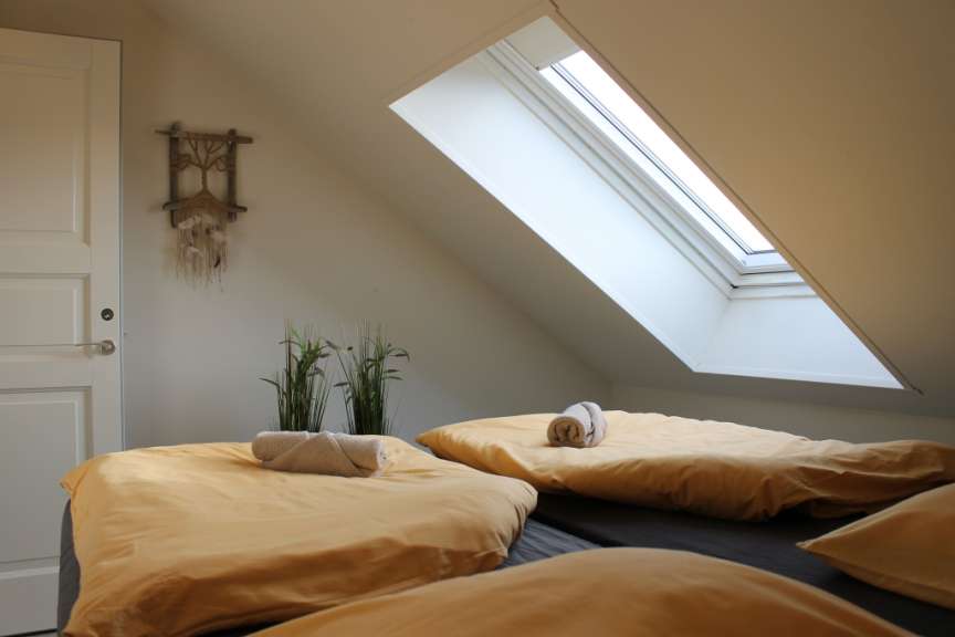 Ein Schlafzimmer mit einem Dachfenster, zwei Betten mit gelber Bettwäsche und einem Traumfänger an der Wand.