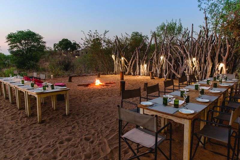 Tische und Stühle im Sand mit einem Feuer im Hintergrund