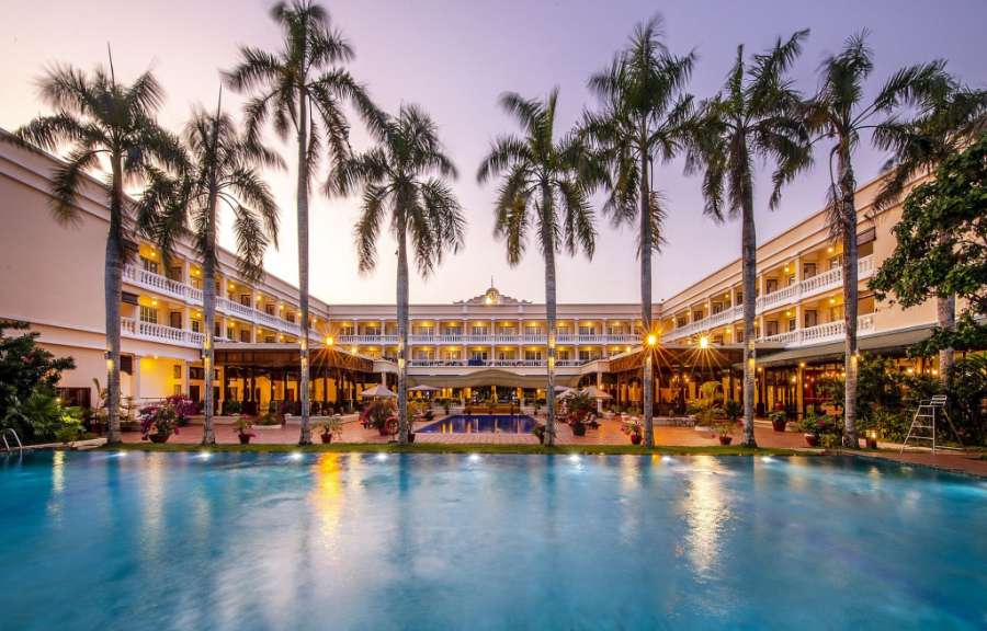 Ein Hotel mit Swimmingpool und Palmen im Abendlicht.