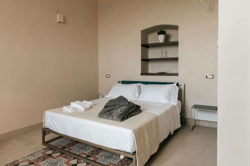 Ein Bett mit weißen Laken und einer grauen Robe steht in einem minimalistisch eingerichteten Schlafzimmer.