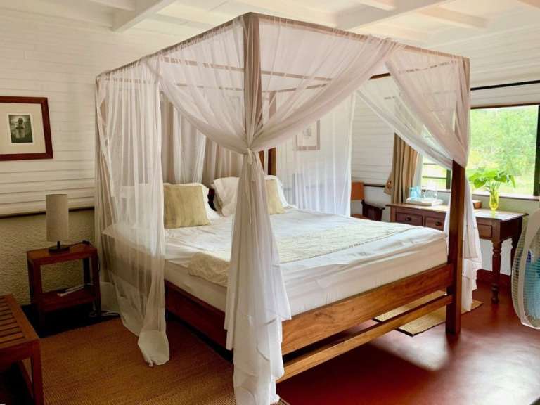 Ein Himmelbett mit weißen Vorhängen steht in einem Zimmer mit Holzboden und einer Wand aus weißen Holzdielen.