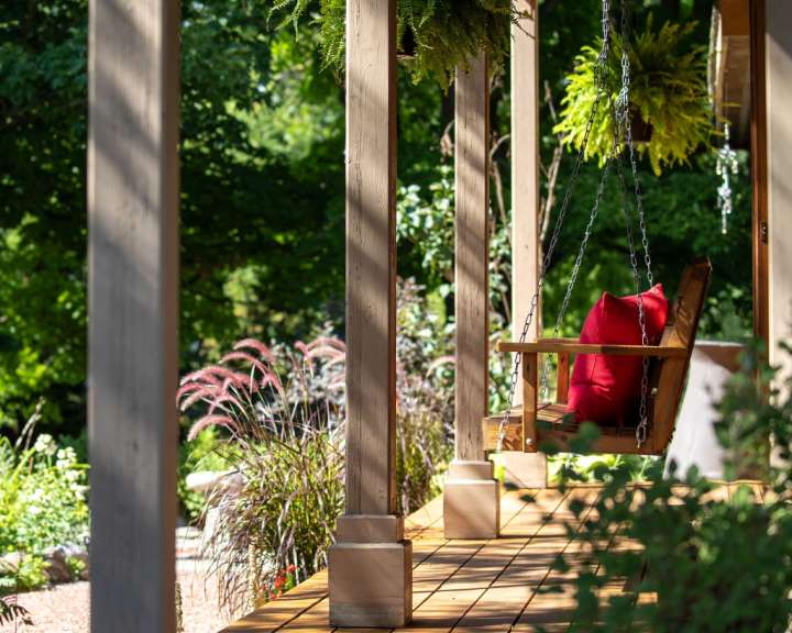Eine Schaukel auf einer Veranda mit einem roten Kissen darauf