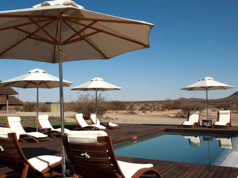 Liegestühle und Sonnenschirme um einen Swimmingpool an einem sonnigen Tag