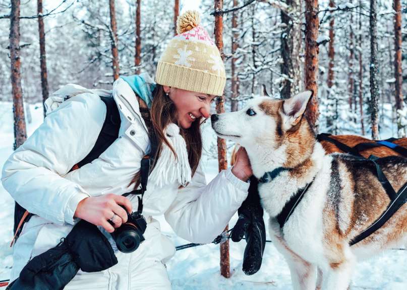Eine Frau hält eine Kamera und streichelt einen Husky-Hund im Schnee
