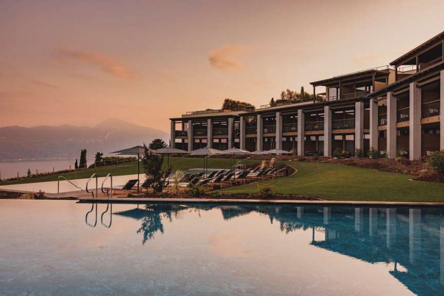 Ein Infinity-Pool spiegelt den Himmel und die Berge in der Nähe eines modernen Hotels mit Terrassen und Liegestühlen wider.