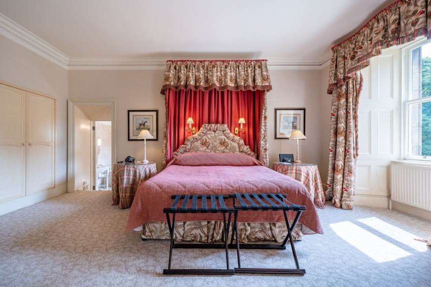 Ein luxuriöses Schlafzimmer mit einem Himmelbett, antiken Möbeln, einem Teppichboden und einem großen Fenster.