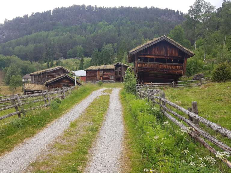 Ein Schotterweg führt zu einem Holzhaus mit Grasdach
