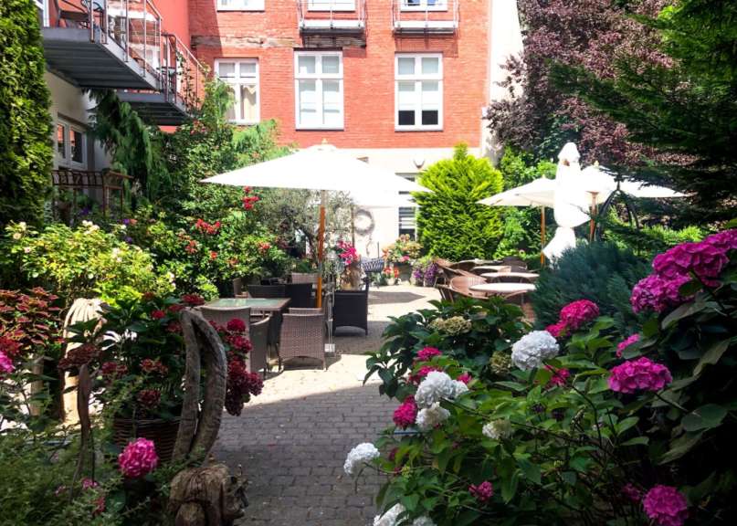 Ein garten mit blumen und tischen und schirmen vor einem roten backsteingebäude