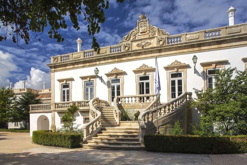 Eine weiße Villa mit einer Steintreppe im Freien steht unter einem blauen Himmel mit Wolken.