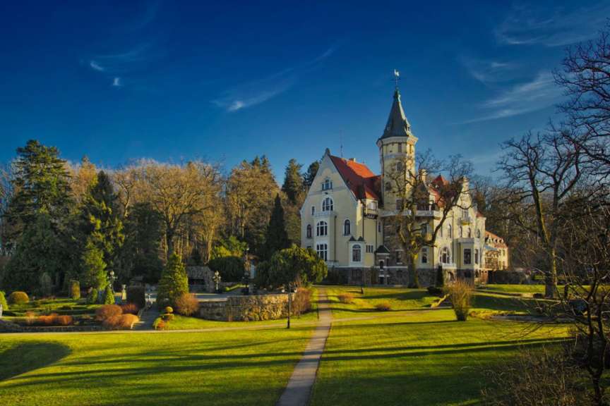 Ein großes weißes Gebäude mit einem roten Dach steht inmitten eines grünen Parks