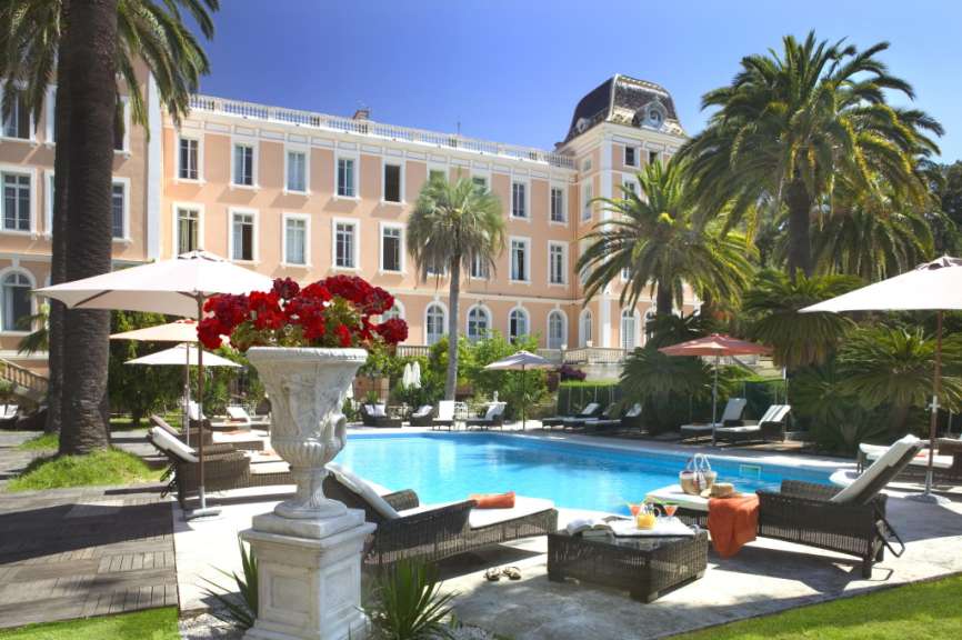Ein großer Pool mit Liegestühlen und Sonnenschirmen vor einem großen Gebäude