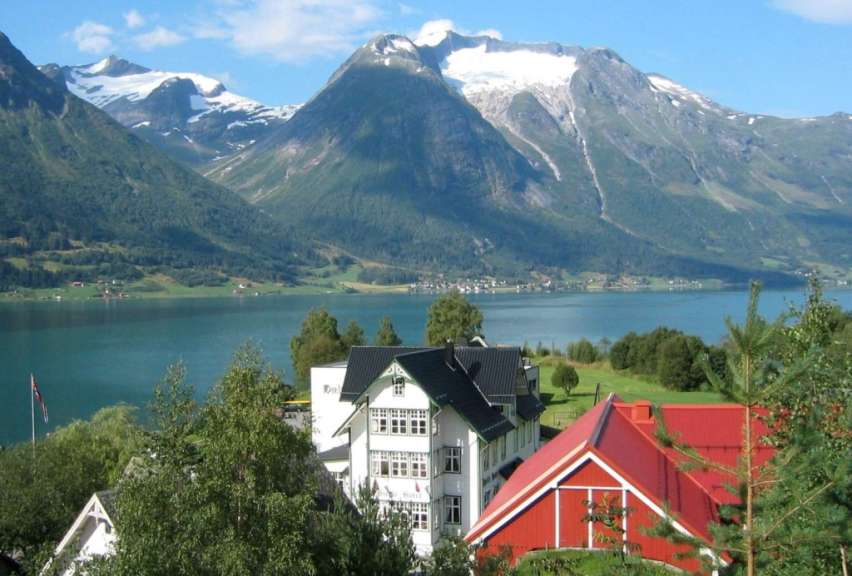 Ein weißes Gebäude mit einem roten Dach steht in der Nähe eines Sees mit Bergen im Hintergrund