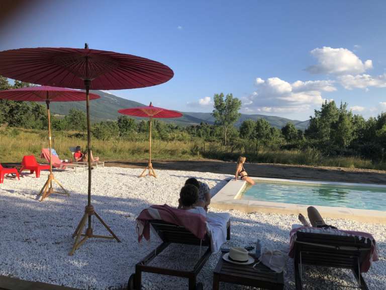 Eine Gruppe von Menschen sitzt neben einem Pool mit Regenschirmen