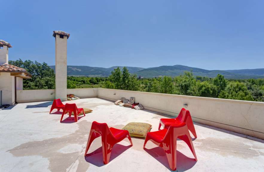 Eine Terrasse mit roten Stühlen und Kissen und Blick auf die Berge