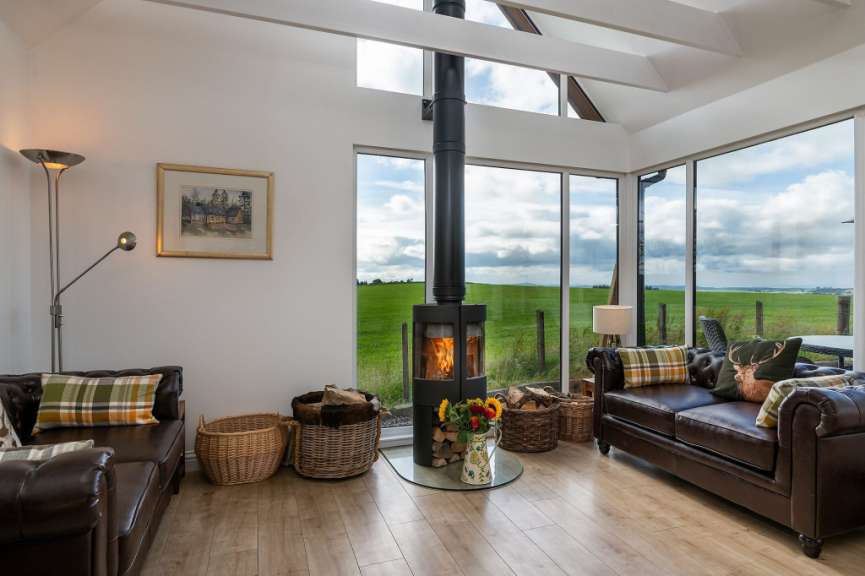 Ein Wohnzimmer mit Kamin und Ledersofas bietet durch große Fenster einen Blick auf eine grüne Landschaft.