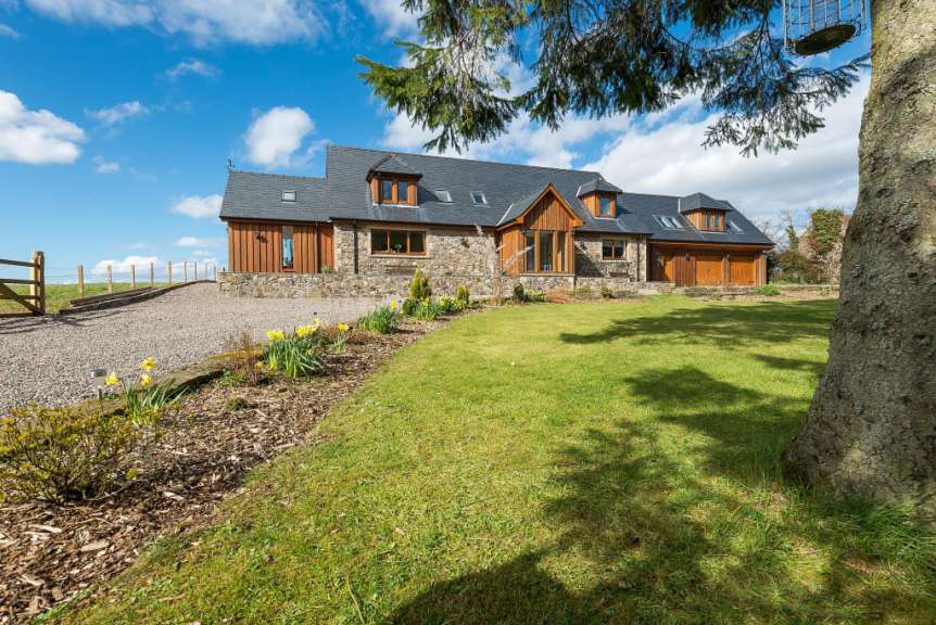 Ein Steinfassadenhaus mit Holzverkleidung und Schieferdach steht unter einem blauen Himmel mit weißen Wolken.