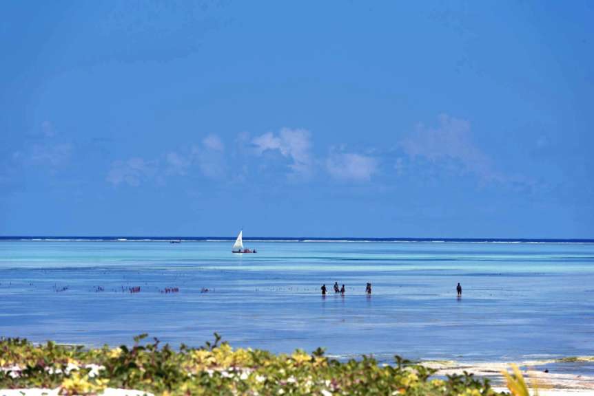 Eine Gruppe von Menschen geht am Strand entlang , während ein Boot im Hintergrund segelt