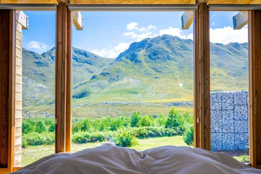 Ein Blick aus einem Zimmer auf grüne Berge und blauen Himmel, mit einem Bett im Vordergrund.